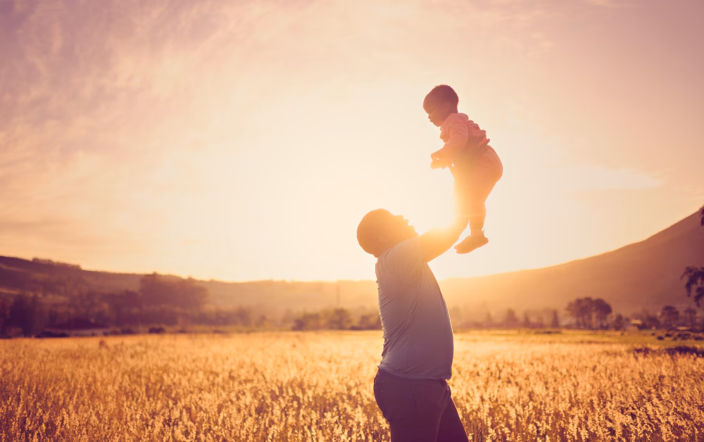 Father lifting young child in a golden field at sunset