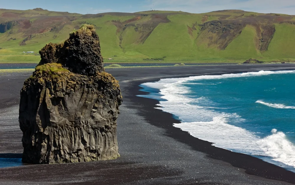 Waves breaking on a black sand beach below jagged mountains in Iceland
